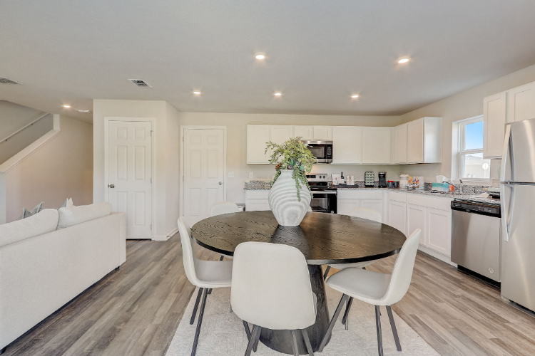 A kitchen with a dining table and white chairs.